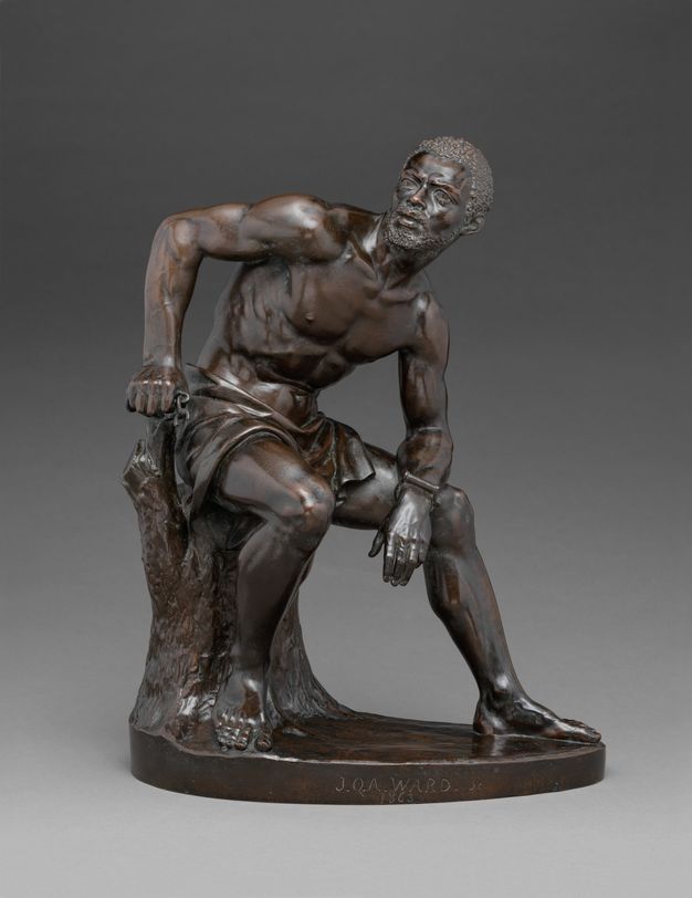 Sculpture. This freestanding statuette is of a muscular Black man wearing only a cloth around his hips and a shackle on one wrist. His sits on a stump and leans forwards onto one knee. His head turns the other direction, and his face is lined.