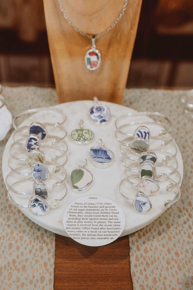 Jewellery. Twelve bracelets and four pendants are made with fragments of white porcelain painted blue, green, or faint red. Each is set into silver. A label on a display tray begins, “chaney Pieces of china (1750-1900) found on the beaches and grounds of old sugar plantations on St. Croix.”